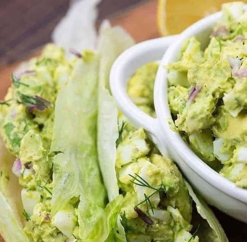 Bowl of avocado egg salad next to lettuce leaves holding more of the salad