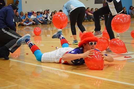 Balloon Pop Pep rally activities can include balloons like this one which shows a boy on the floor of a gym trying to pop an orange balloon.