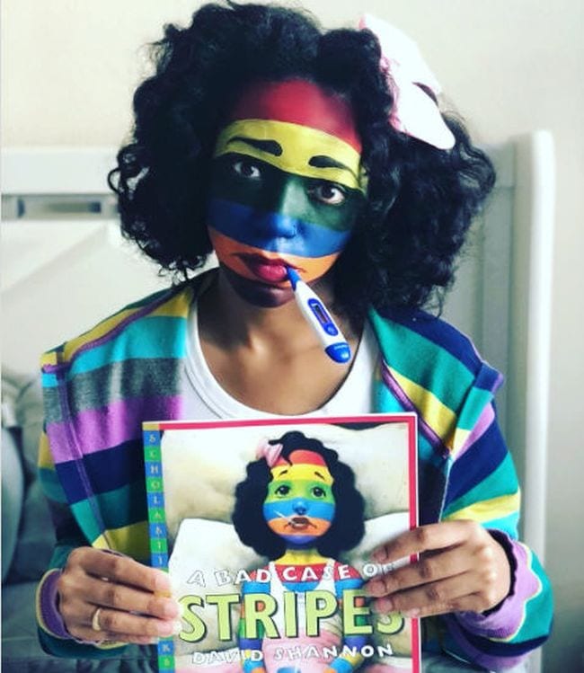 Woman with her face painted in colorful stripes and a thermometer in her mouth, holding A Bad Case of Stripes- book character costume