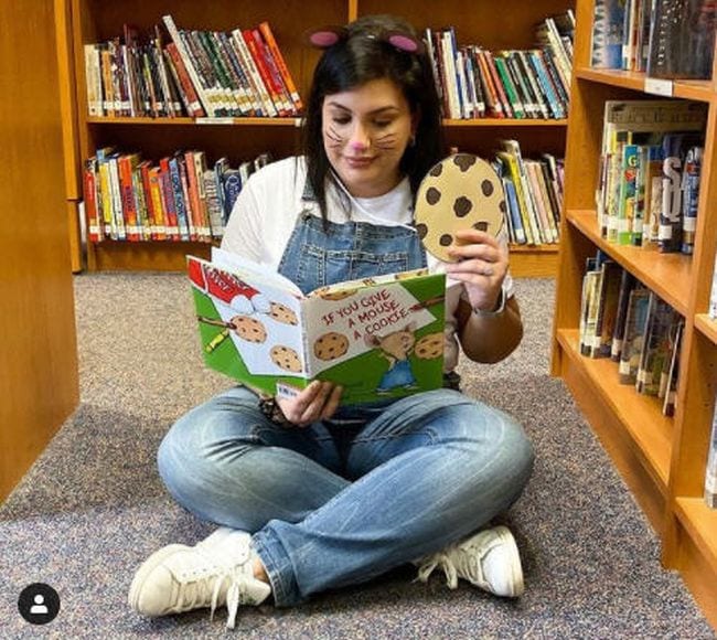 Book Character Costume Ideas Mouse Cookie Woman in blue overalls and mouse ears holding a large paper cookie and reading a book (Book Character Costume Ideas)