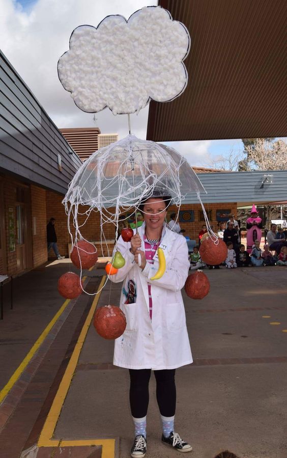Cloudy with a Chance of Meatballs A woman is wearing a white lab coat and holding a clear umbrella that has a cloud coming out of it. There are meatballs and other food items hanging from the umbrella.