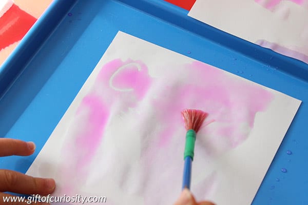 Crayon-resist-letters-3 A piece of paper with pink paint and white letters underneath with a paintbrush laying on top