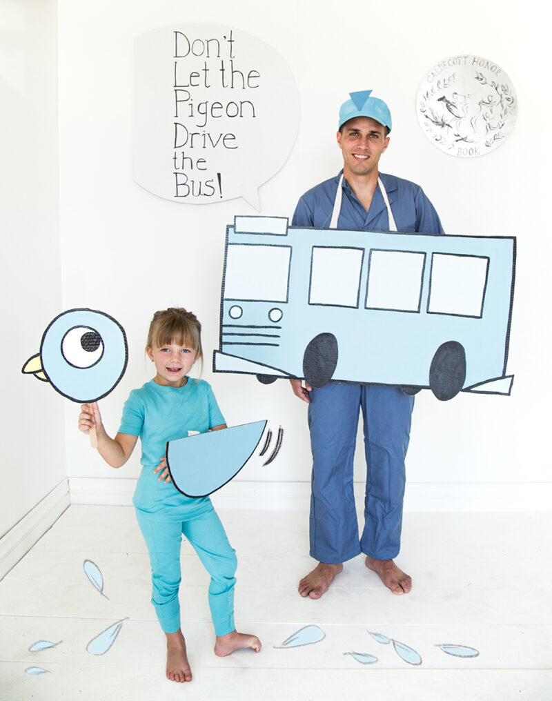 Don’t Let the Pigeon A sign reads Don't let the pigeon drive the bus. a man is wearing blue and standing behind a cutout of a bus. A child is also dressed in blue and holding a pigeon head cut out.