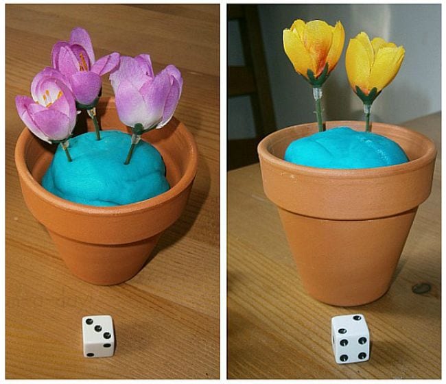 First grade math games using flower pots with playdough soil, filled with artificial flowers matching the number shown on the dice nearby