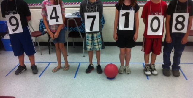 Students wearing numbers, lined up with a playground ball used to represent a decimal