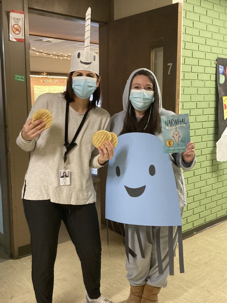 Two women are shown one dressed as a narwhal and the other as a jellyfish. They are holding waffles.