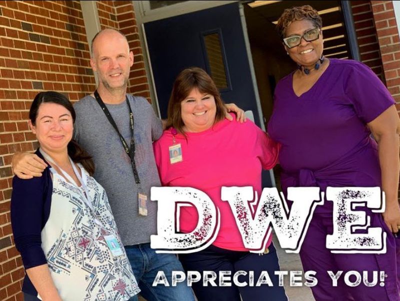 National Custodian Day Four members of a school custodial staff gathered in front of the school, with a note saying DWE appreciates you, in honor of National Custodian Day