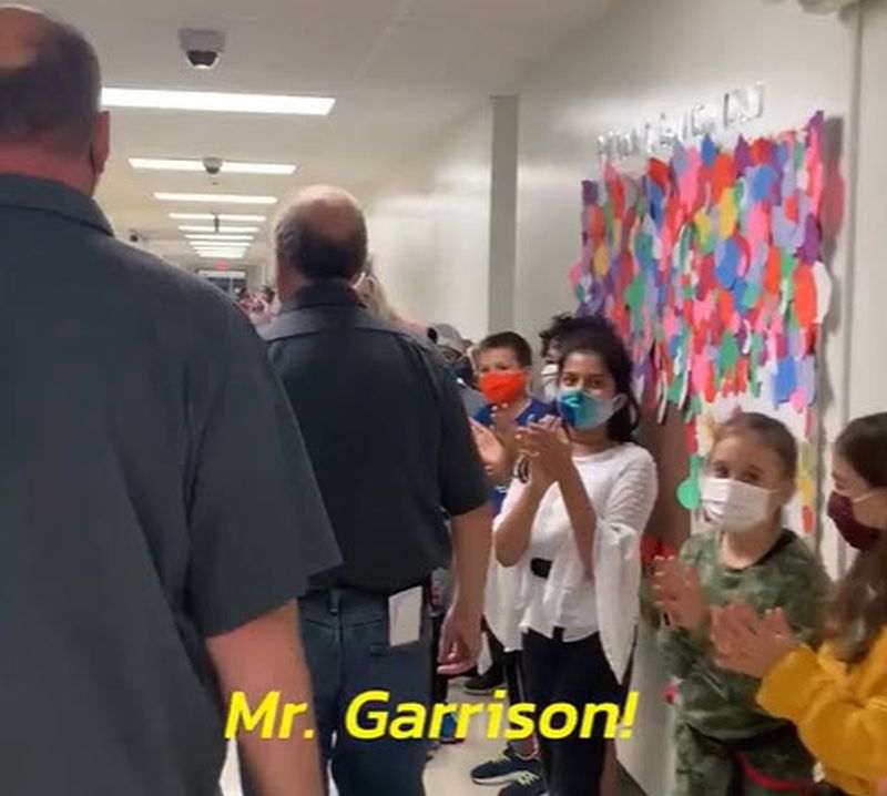 National Custodian Day School custodians walking through a hallway filled with students thanking them for their hard work. Text reads Mr. Garrison!