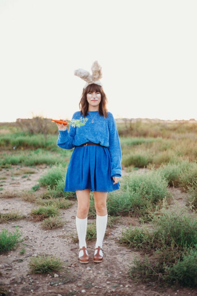 Peter Rabbit A woman is shown wearing bunny ears, holding a carrot, with bunny face paint and dressed in blue.