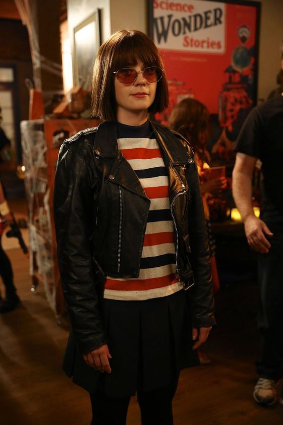 ramonaquimby A woman is seen wearing a black skirt and jacket and a black, red, and white striped shirt. She is also wearing sunglasses and has a short bob haircut with bangs.