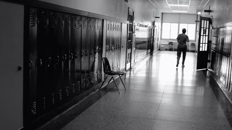 Black and white photo of a teacher in a hallway with lockers--let's stop teacher blame