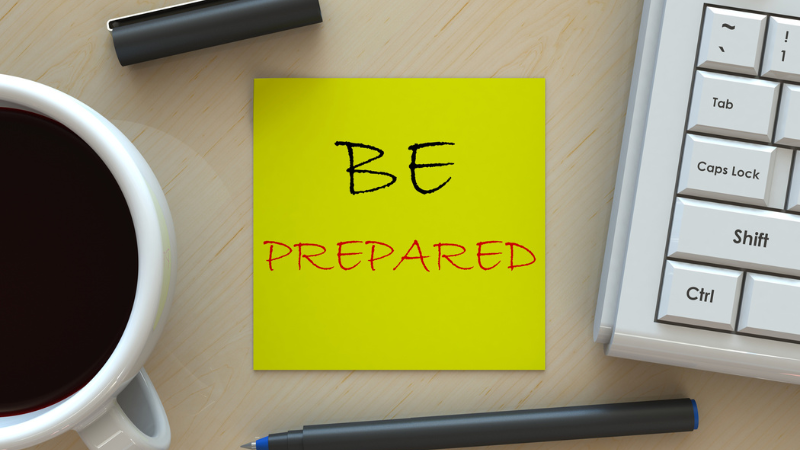 Yellow sticky note on desk with coffee, ben and keyboard that says Be Prepared.